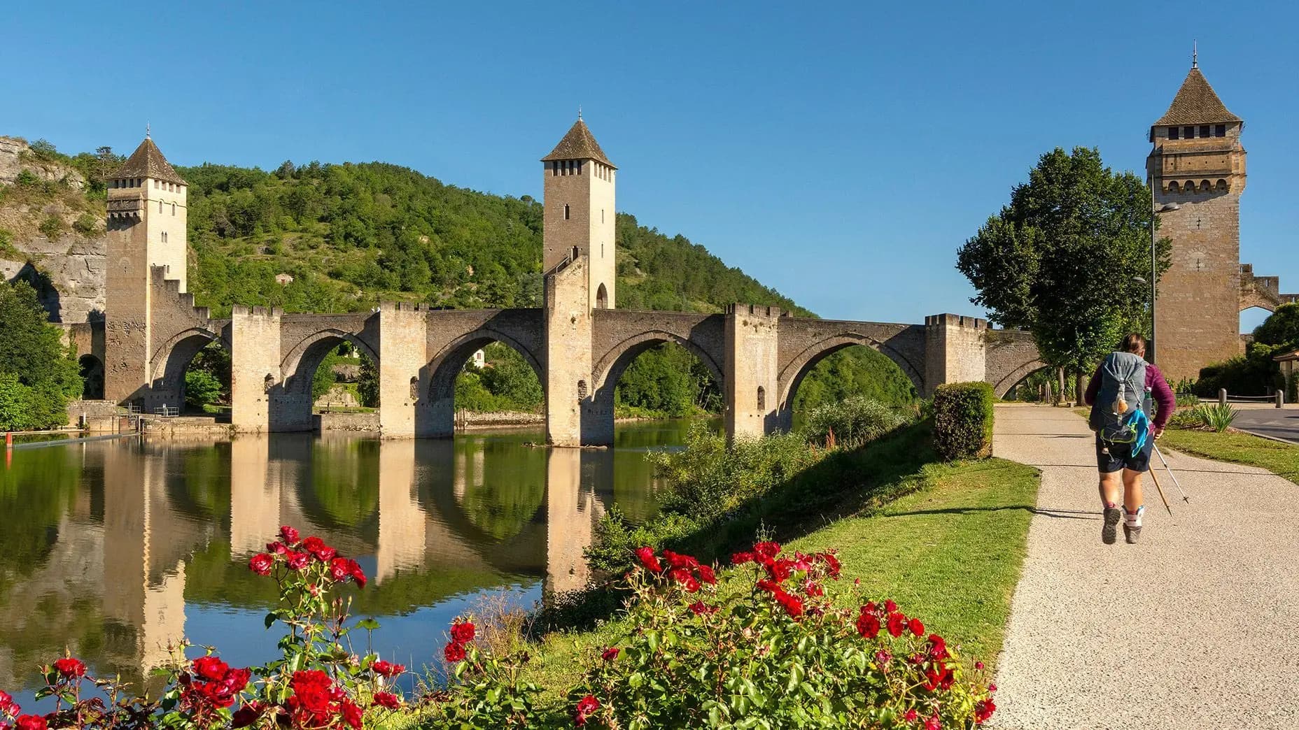 Peregrina con mochila y bastones cruzando el Pont Valentré de Cahors, en la ruta francesa del Camino de Santiago
